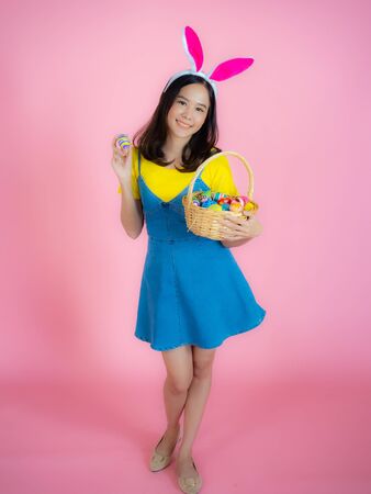 Portrait of a happy young woman wearing Easter bunny ears prepares to celebrate Easter on a pink background.の写真素材