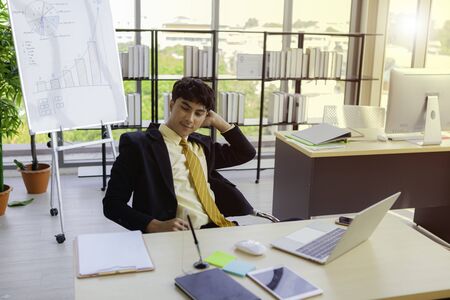 A young businessman is sitting down for a short break from hard work throughout his work hours to relieve stress and create new ideas from working in the workplace.の写真素材
