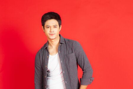 A portrait of a young hipster man making a curious face while shooting on a red background.の写真素材