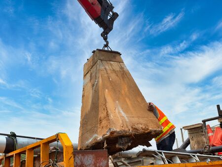Workers are controlling the direction of the foundation pillar that is lifted by a crane mounted on a truck to be placed on a space on the back of the pickup truck and placed on the construction site.の写真素材