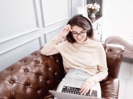 Smiling young woman enjoying music through headphones with laptop in living roomの写真素材