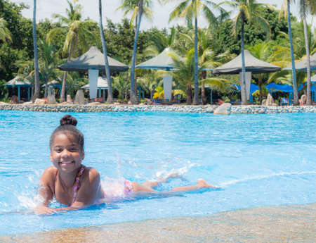 Portrait of Cute little girl African-American in swimming suit sitting in a water pool on a summer day.の写真素材