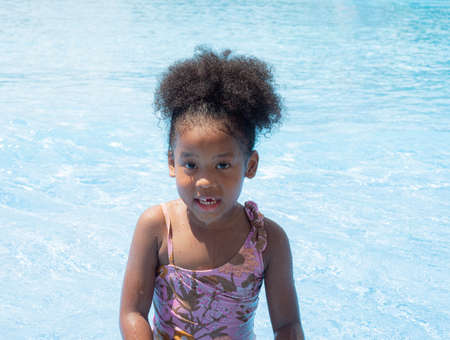 Portrait of Cute little girl African-American in swimming suit sitting in a water pool on a summer day.の写真素材