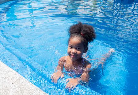 Portrait of Cute little girl African-American in swimming suit sitting in a water pool on a summer day.の写真素材