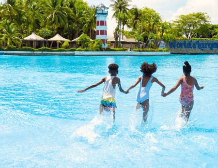 Summer season. Three African American children having fun on the swimming pool in aqua park at the day time. Fun and summer lifestyle.の写真素材