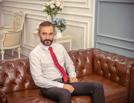 An executive businessman with a beard sitting in hotel lobby waiting for someoneの写真素材