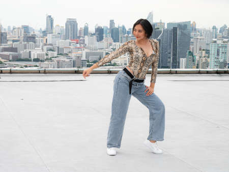 A female hip hop dancer in a snakeskin costume is dancing happily at the top of a high-rise building.の写真素材
