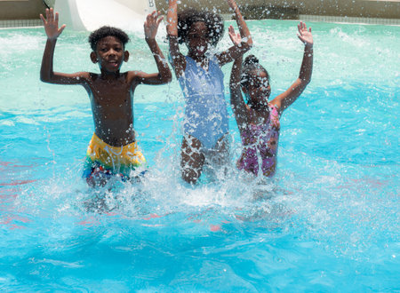 Summer season. Three African American children having fun on the swimming pool in aqua park at the...