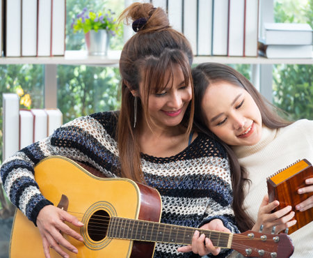 Young Asian lesbian couple intending to play a musical instrument together, guitar and kalimba, in the living room at home, the lifestyle of couple LGBT loving women happy in romantic love and funの写真素材