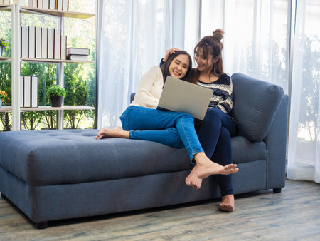 Beautiful young Asian women LGBT lesbian couple happy couple sitting on the sofa in the living room, using the laptop computer bought online at home. LGBT lesbian couple together indoors conceptの写真素材