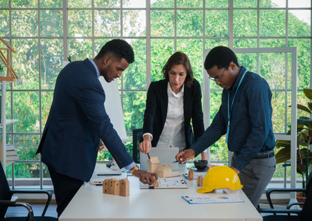 Businesspeople's multiracial colleagues brainstorm with house models and blueprints at the office. Professional construction team discussing the arrangement of service lines at the new building.の写真素材