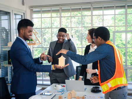 Businesspeople's multiracial colleagues brainstorm with house models and blueprints at the office. Professional construction team discussing the arrangement of service lines at the new building.の写真素材