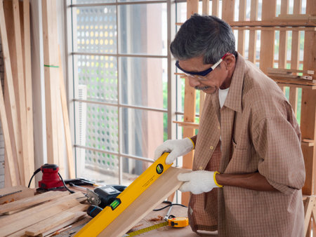 Accuracy and quality. Happy senior carpenter checking the level of a plank of wood. Measurement conceptの写真素材