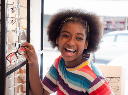 African girl in the optic store looking in the mirror for choosing a new eyeglasses frame. health care, medicine, people, eyesight and technology conceptの写真素材