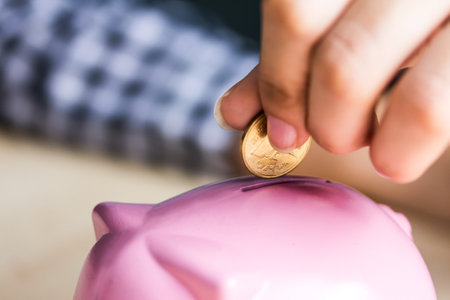 closeup women hand putting coin into a piggy bank  in finance banking and saving conceptの写真素材