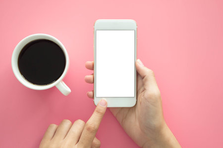 man hold blank display smartphone Modern pink office desk with laptop and other supplies with cup of coffee for input the text on copy space Top view, flat lay.の写真素材