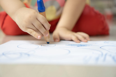 Close up hand of 2 years kid use color pencil draw line on paper. Concept of art for children...