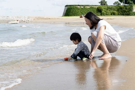 Mother and 3 years old asian kid play sand on the beach. Background for family life and education. holiday with children.の写真素材