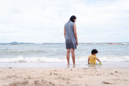 Mother and 3 years old asian kid playing on the beach. Background for family vacation and recreation.の写真素材