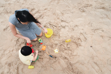 Mother and 3 years old asian kid play sand on the beach. Background for family life and education. holiday with children.の写真素材