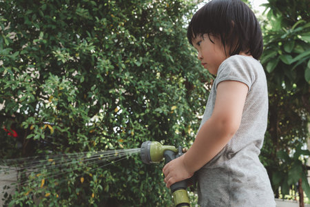 Funny moment of 3 Year old asian kid playing water with garden hose in backyard. Background concept ...