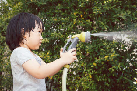 Funny moment of 3 Year old asian kid playing water with garden hose in backyard. Background concept  for play time and summer of children.の写真素材