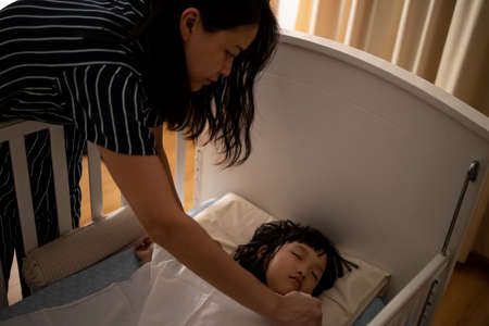 Close up asian mother tuck the blanket on kid sleep in bed. Concept for family connection and relationship.の写真素材