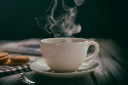 White coffee cup and coffee with smoke and cookies on old wooden background.