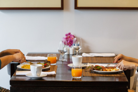 A couples, women and men seating to eat breakfast and drinks, with both orange juice and coffee on the tableの写真素材