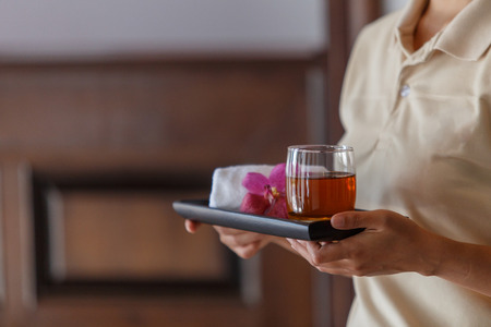 The woman serving welcome drink there were  cold water with cool cloth and beautiful orchid flowers on the small trayの写真素材