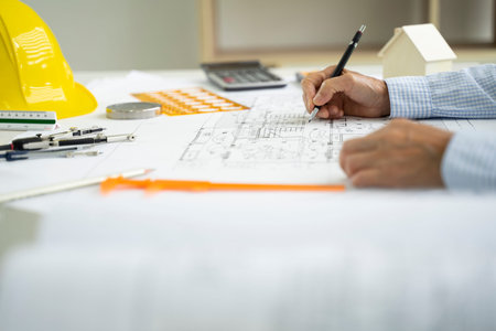 Architect hands working on blueprint plans  with  a pencil,  a ruler, calculator, smartphone, laptop...