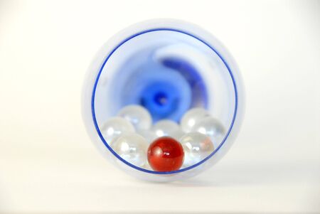 The top view of some white marbles and a red marble inside a blue glass.の写真素材