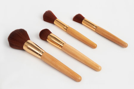 Four professional makeup brushes with soft brown bristles, wooden handles, and golden ferrules are arranged on a clean white background, ready for beauty applicationの写真素材