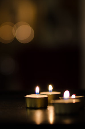 Warm and serene close-up of lit tealight candles in a dim setting. The soft bokeh lights in the background add to the peaceful ambiance, perfect for meditation or relaxation themes.の写真素材