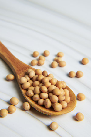 Soybeans resting in wooden spoon on white wooden table, creating a rustic and healthy imageの写真素材
