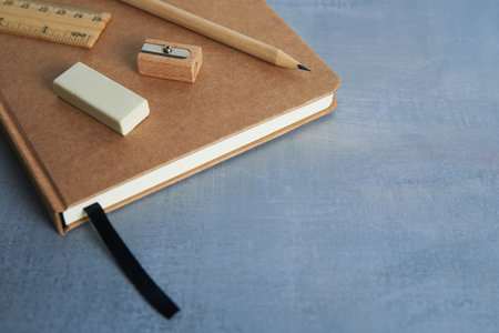 Brown notebook with pencil, eraser, ruler, and sharpener on blue background, simple stationery arrangement for study or work.の写真素材