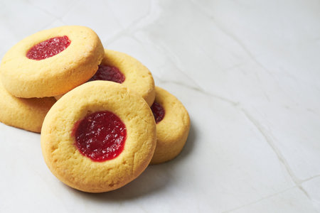 Freshly baked thumbprint cookies with a vibrant raspberry filling are presented on a clean marble surfaceの写真素材