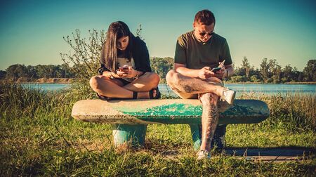 couple  sitting on park bench with their mobile phonesの写真素材