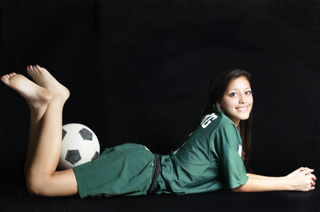A soccer teenager player posing for a portrait with her ball in a black backgroundの写真素材