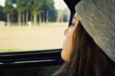 Pensive teenage girl  looking out window carの写真素材