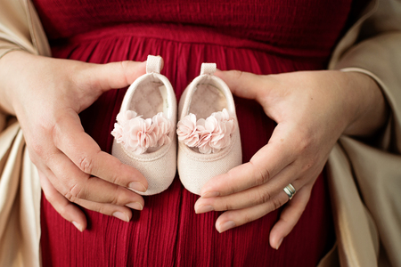 Pregnant woman maternity picture of her belly with a pink little shoesの写真素材