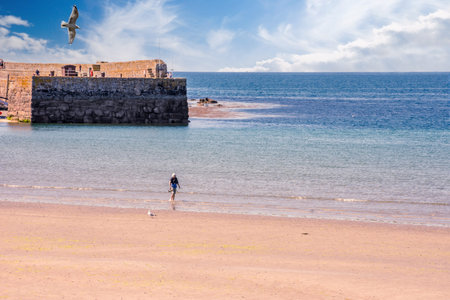 25 July 2018: Marazion, Cornwall, UK-Tourists walk along the beaches of Marazion, an ancient market town in Cornwall, England.のeditorial素材