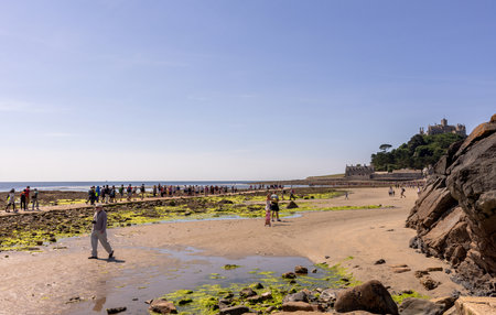 25 July 2018: Marazion, Cornwall, UK-People walking on the causeway across to St Michaels Mount in Cornwall Britain. At low tide, the island can be reach by foot from Marazion town by a man-made causeway.のeditorial素材