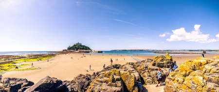 25 July 2018: Marazion, Cornwall, UK-People walking on the causeway across to St Michaels Mount  in Cornwall Britain. At low tide, the island can be reach by foot from Marazion town by a man-made causeway.のeditorial素材