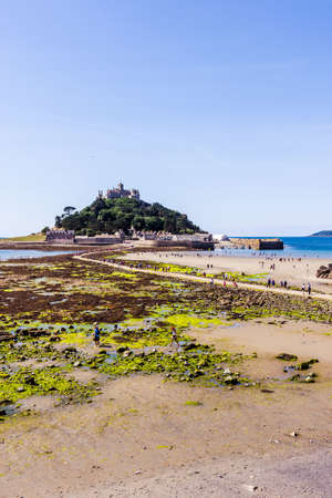 25 July 2018: Marazion, Cornwall, UK-People walking on the causeway across to St Michaels Mount in Cornwall Britain. At low tide, the island can be reach by foot from Marazion town by a man-made causeway.のeditorial素材
