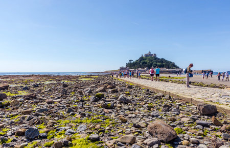 25 July 2018: Marazion, Cornwall, UK-People walking on the causeway across to St Michaels Mount in Cornwall Britain. At low tide, the island can be reach by foot from Marazion town by a man-made causeway.のeditorial素材