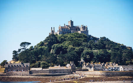 25 July 2018: Marazion, Cornwall, UK-People walking on the causeway across to St Michaels Mount in Cornwall Britain. At low tide, the island can be reach by foot from Marazion town by a man-made causeway.のeditorial素材