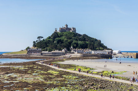 25 July 2018: Marazion, Cornwall, UK-People walking on the causeway across to St Michaels Mount in Cornwall Britain. At low tide, the island can be reach by foot from Marazion town by a man-made causeway.のeditorial素材