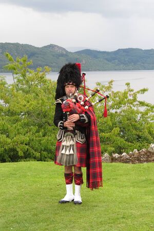 URQUHART CASTLE, SCOTLAND, UK - CIRCA AUGUST 2015: Scottish bagpiper dressed in traditional red and black tartan dressのeditorial素材