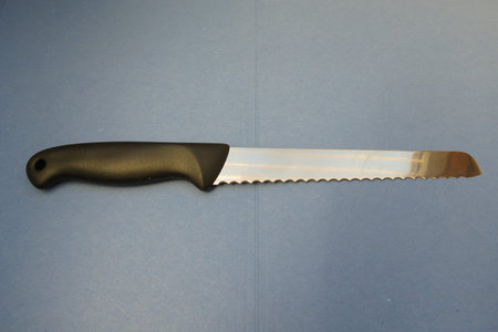 Bread knife with black plastic handle over blue paperboard background